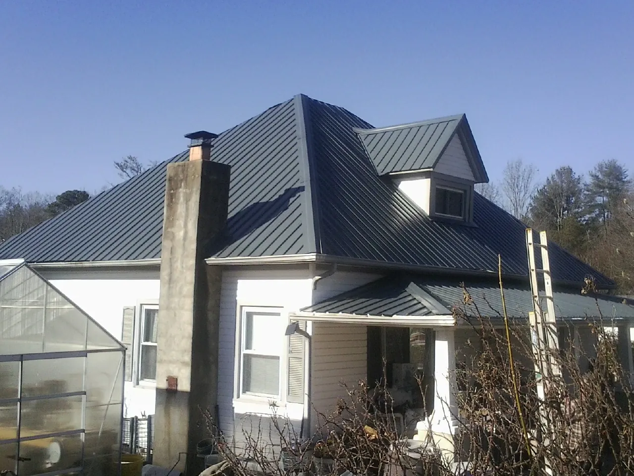 Dark blue standing seam metal roof on a white farmhouse with dormer — Slate & Tile Roof Repair by Roofing Brothers in Glenbrook