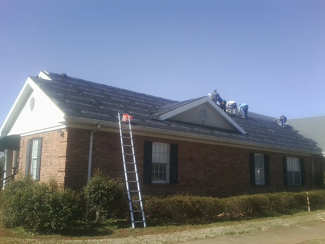 Crew tearing shingles off a brick ranch roof with a ladder set — Metal Roof Repair work by our crew in Glenbrook