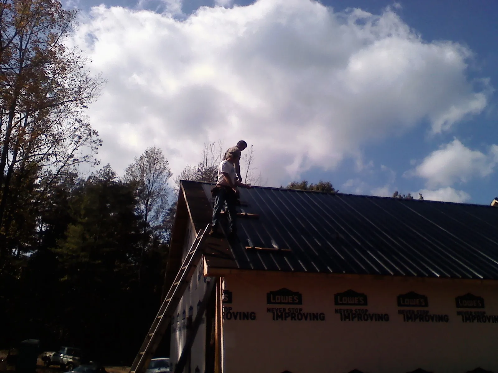 Roofer fastening dark metal panels high against a cloudy sky, from a Roof Inspection job in Glenbrook